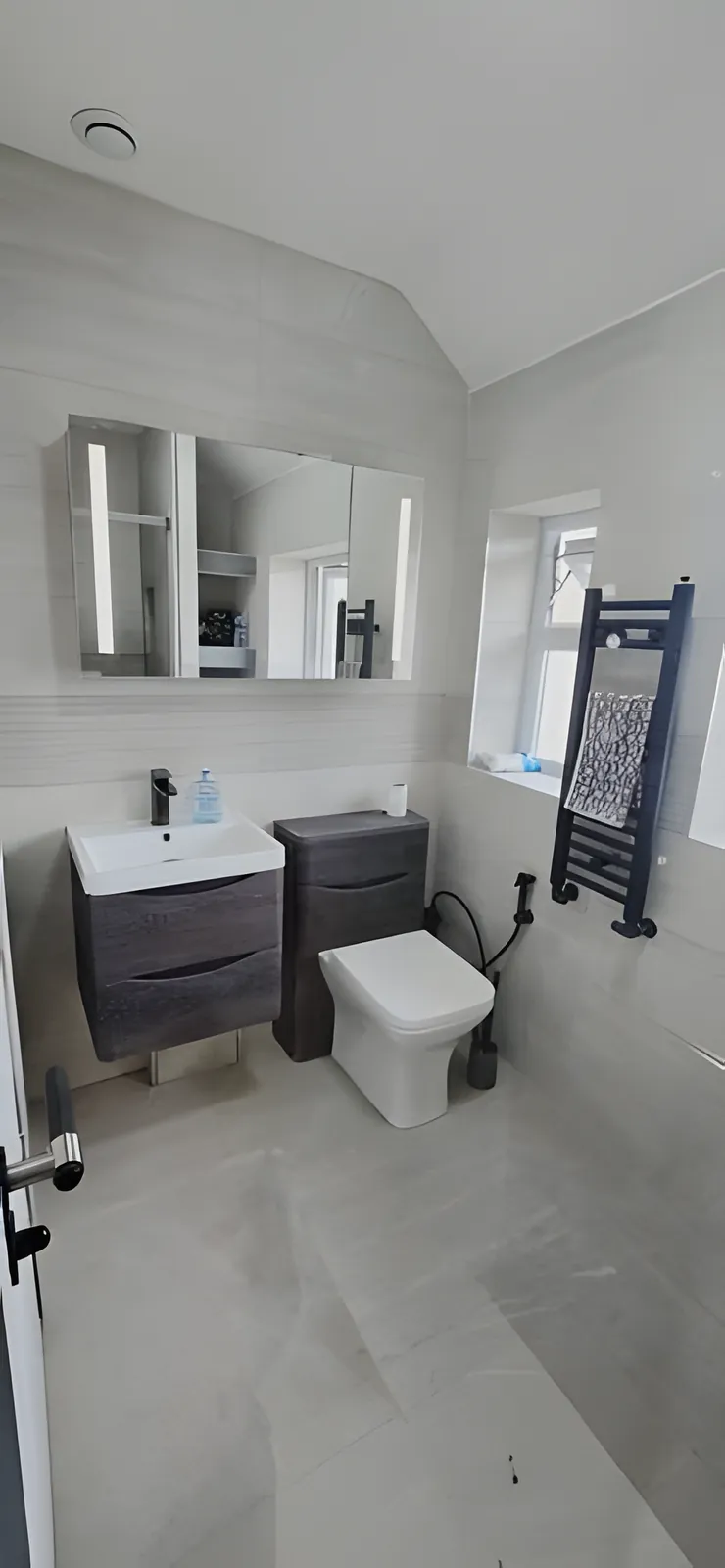 Finished bathroom with an illuminated mirror, vanity unit and towel radiator