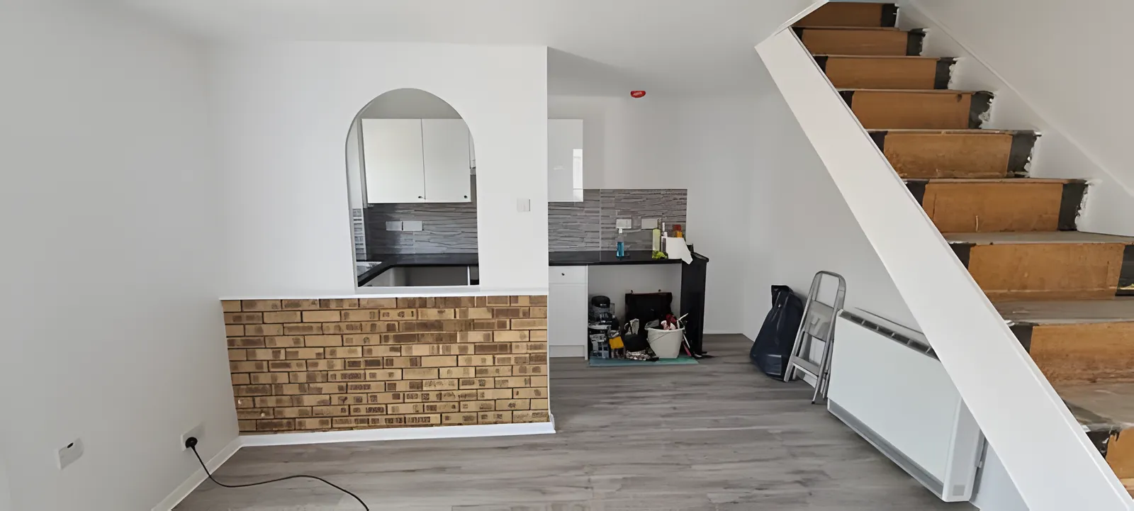 The finished room with white walls, grey flooring and the brick-effect half wall kept as a feature