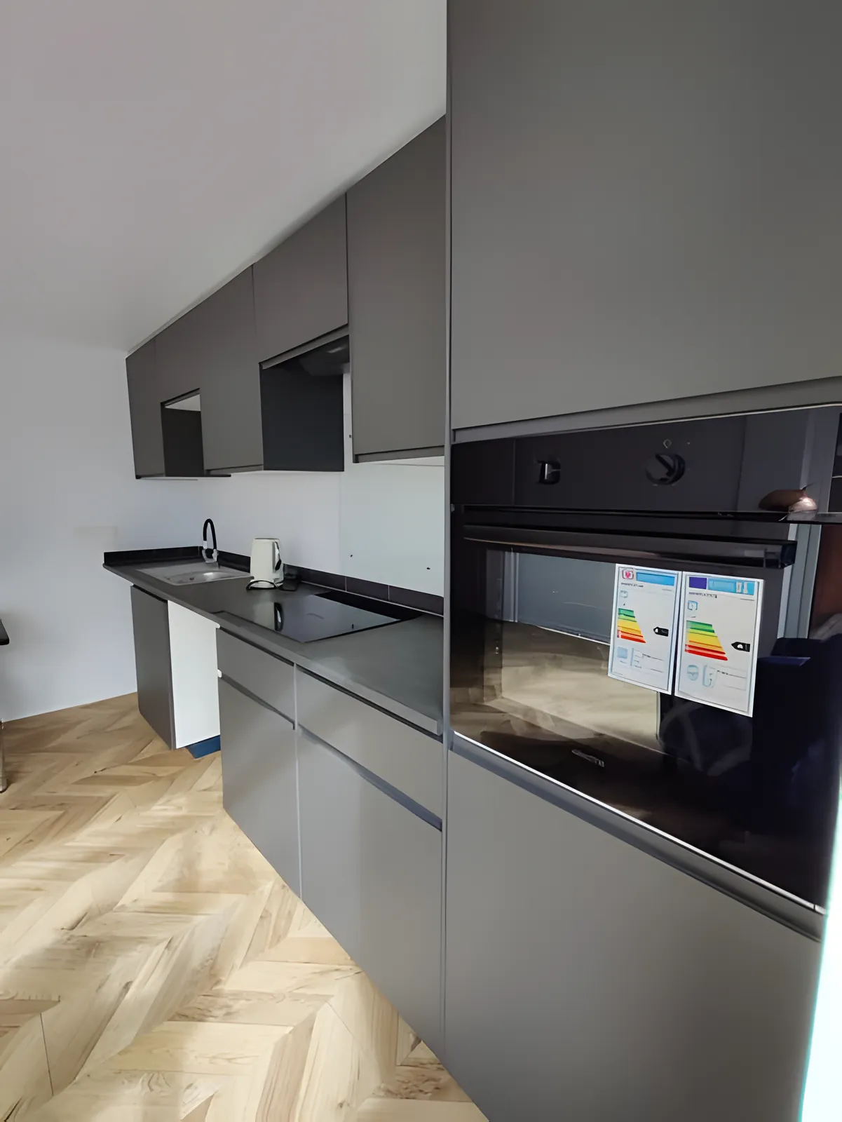 Grey handleless kitchen with a built-in oven and herringbone floor