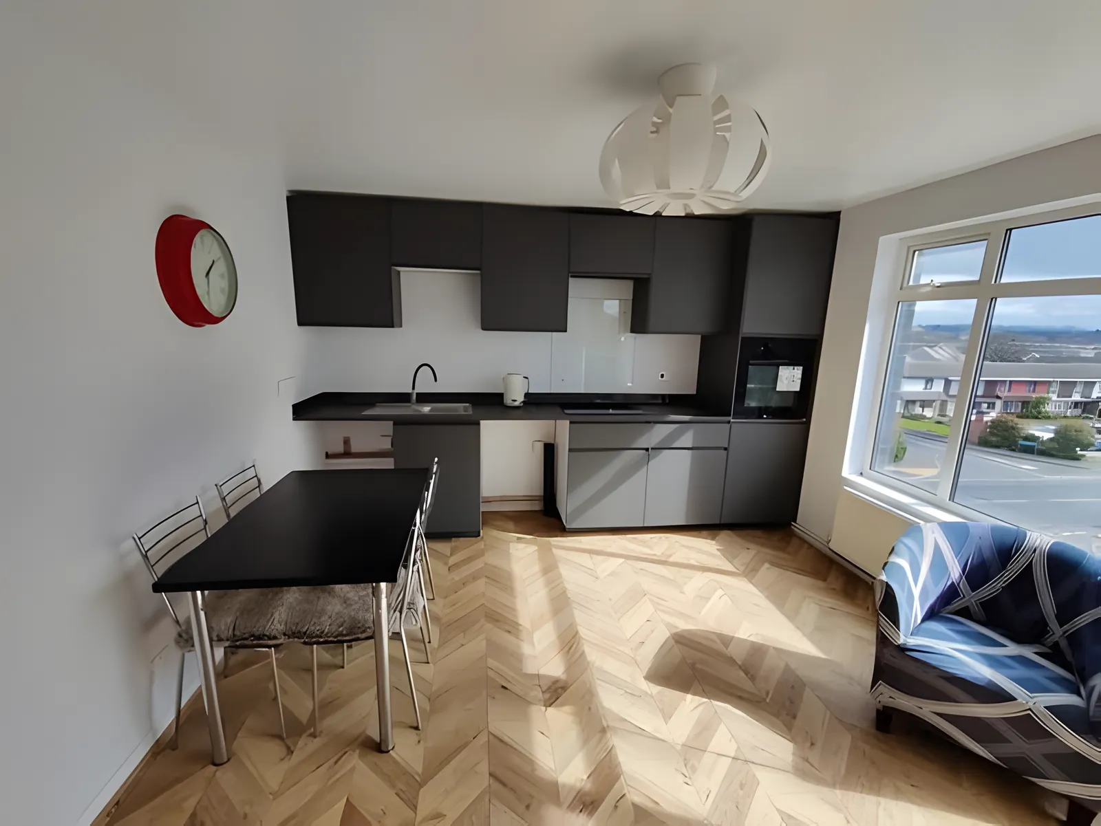 Kitchen-diner with herringbone flooring, dark units and a dining table by the window